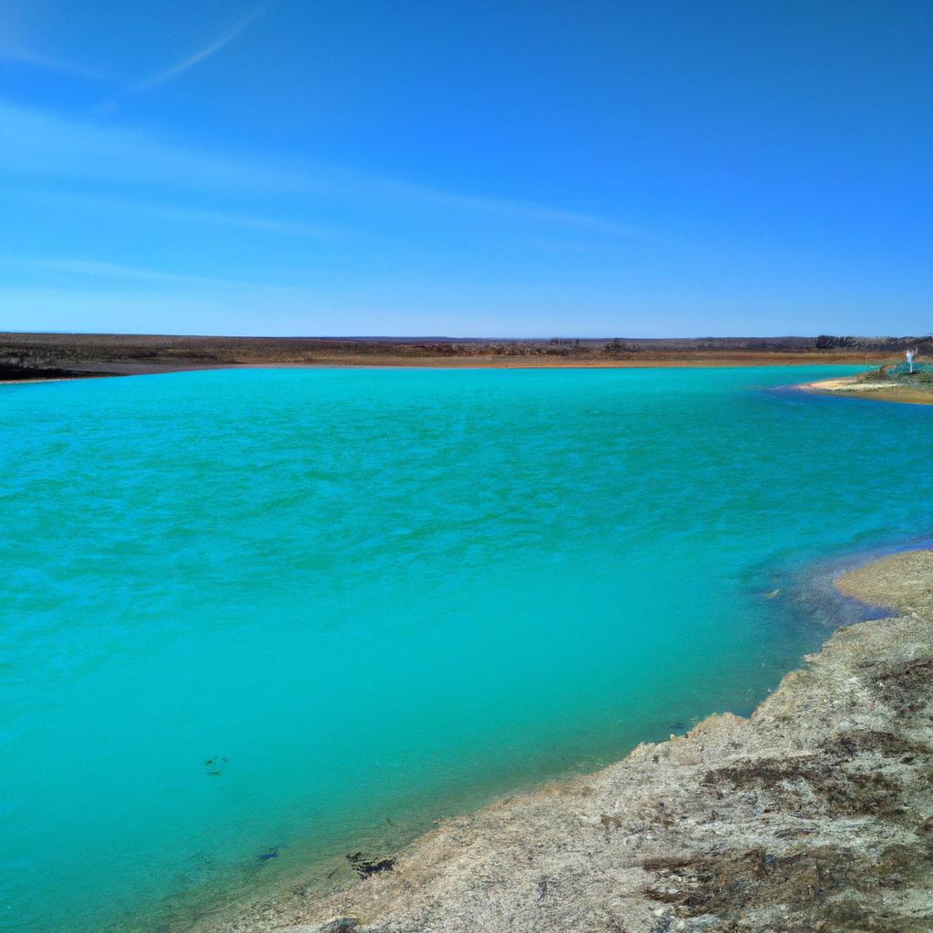 The turquoise blue color of this pond looks stunning against the blue sky, creating a picturesque view.